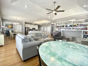 A modern living room with a marble table, grey sofas, and a kitchen in the background.