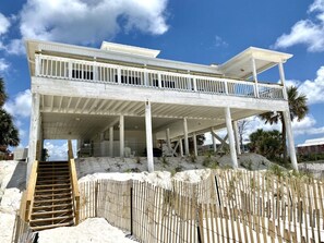 A beachfront house with a covered porch and a wooden staircase leading to the entrance.