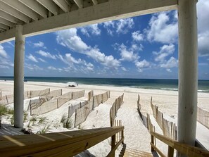 A beach view with a wooden fence and a white car on the sand.