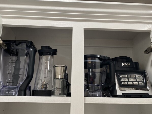 A kitchen cabinet with two blenders and a coffee maker.