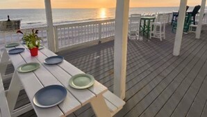 Eine Holzterrasse mit gedecktem Tisch, mit Blick auf den Ozean bei Sonnenuntergang.