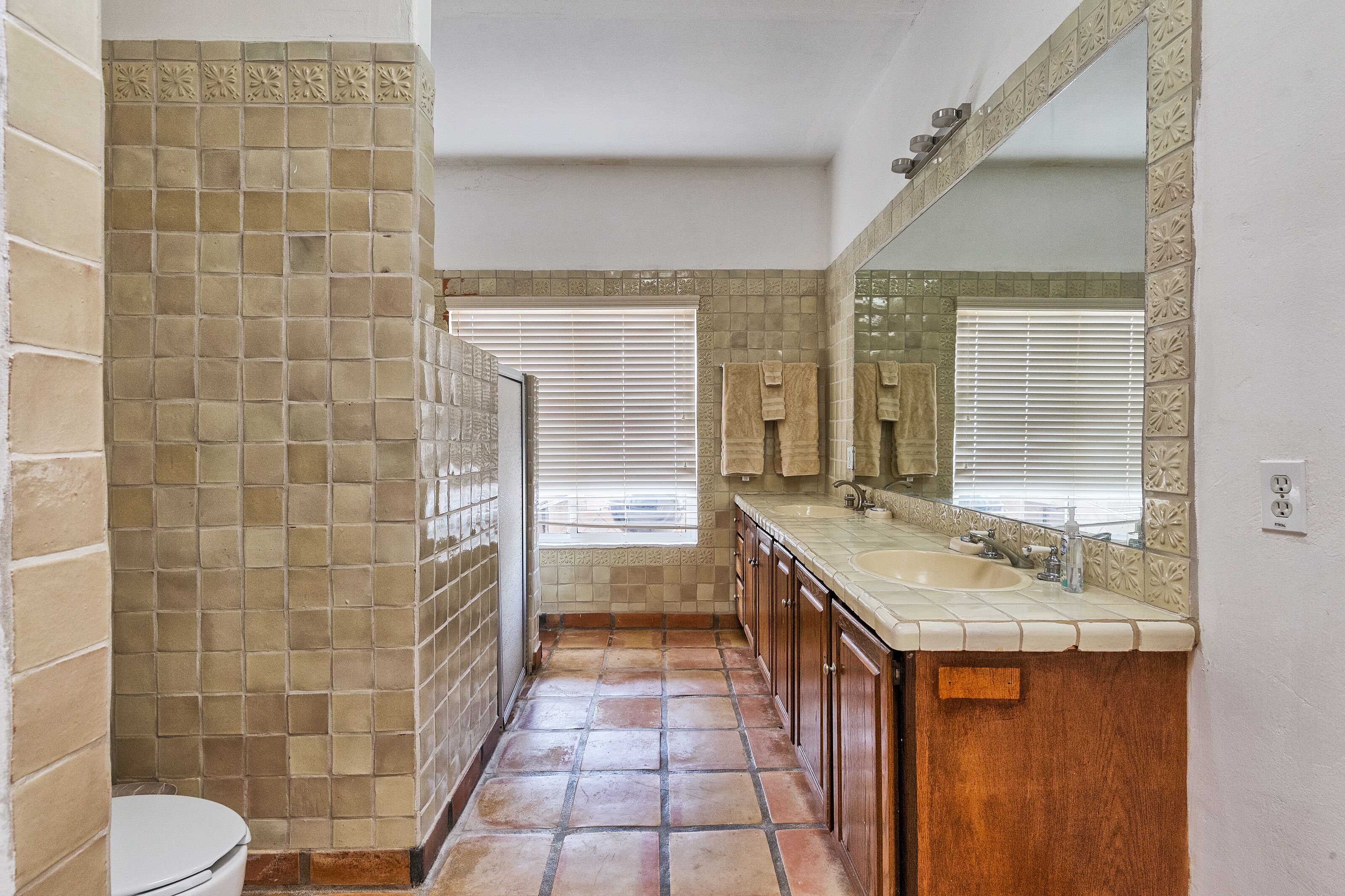 A bathroom with a tiled floor, a sink, a mirror, and a toilet.