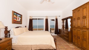 Un dormitorio con una cama grande, un armario de madera y vista al mar a través de un ventanal corredero.