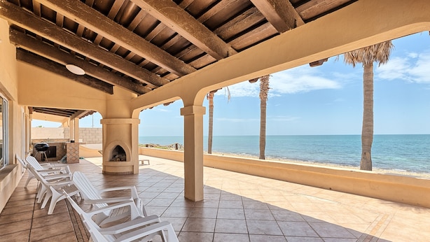 Un patio al aire libre con sillones blancos, una chimenea de piedra y vistas al océano.