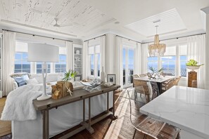 A spacious room with a large dining table, a cozy seating area with a white sofa, and a view of the ocean through large windows.