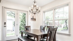 Une salle à manger avec une grande table, quatre chaises, un banc et un lustre.