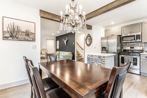 A modern kitchen with stainless steel appliances, a wooden dining table, and a chandelier. - La Casa Negra - Spanish Townhome in SoBro (Indianapolis)