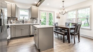 Une cuisine moderne dotée d’un îlot central, de meubles gris et d’un coin repas avec une table et des chaises en bois foncé.