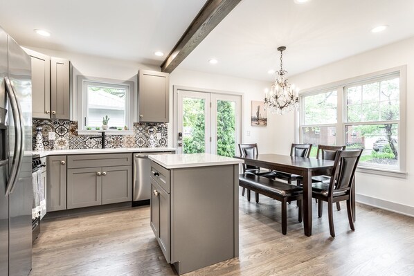 A modern kitchen with a central island, grey cabinets, and a dining area with a dark wooden table and chairs. - La Casa Negra - Spanish Townhome in SoBro (Indianapolis)