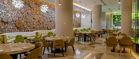 A modern restaurant with round tables, beige chairs, and a wall decorated with wooden logs.