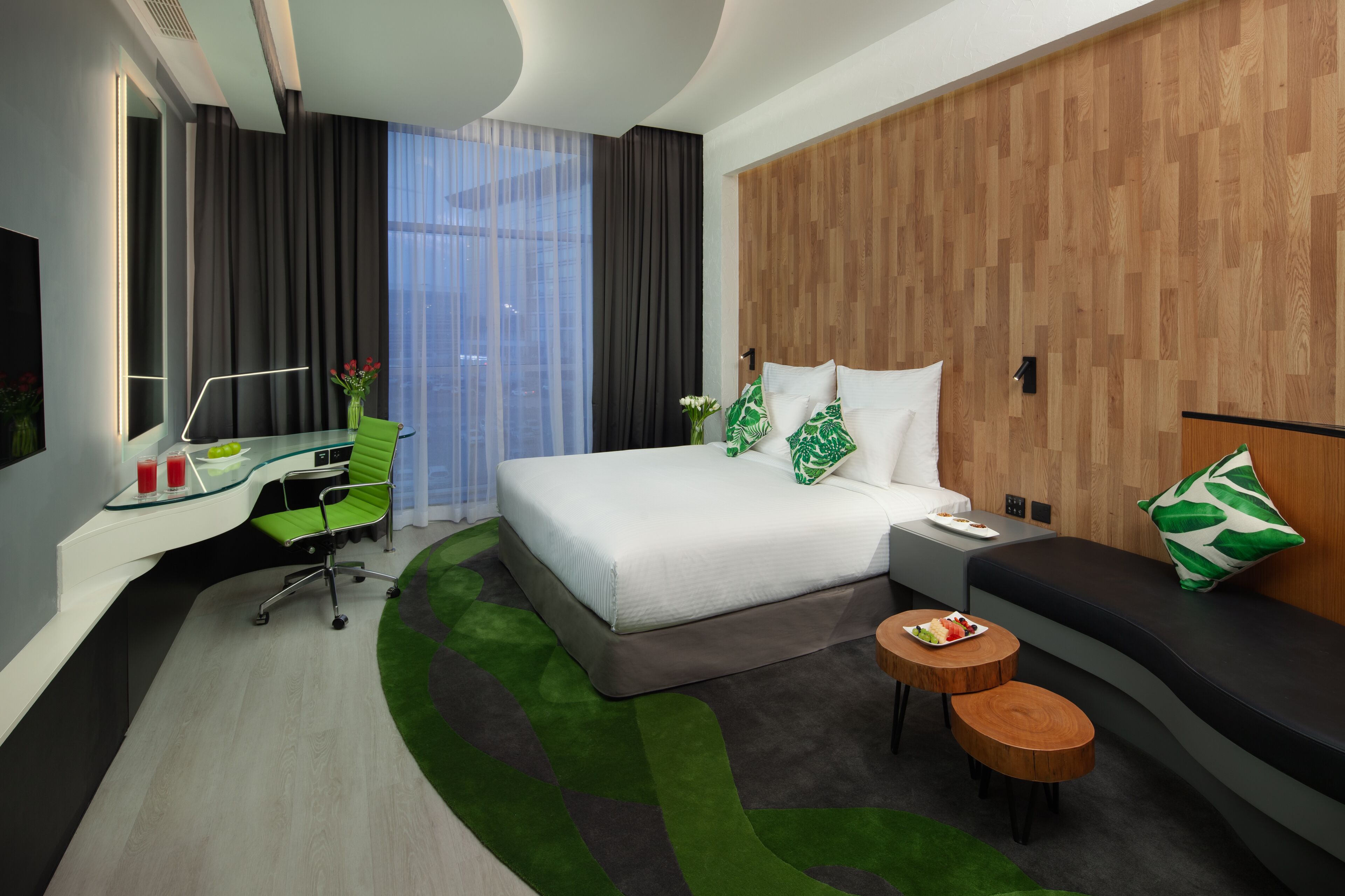 A modern hotel room with a bed, a desk, a sofa, and a small table.