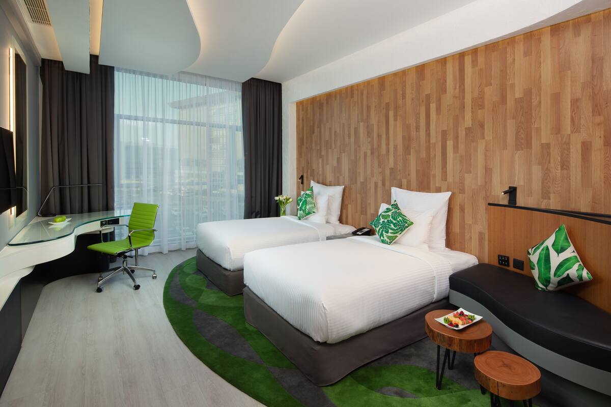 A hotel room with two beds, a desk, a chair, and a small seating area with a table.