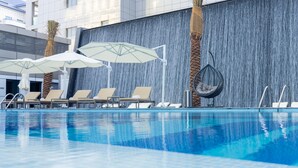 En swimmingpool med liggestole og parasoller, en vandfaldsvæg og palmer.