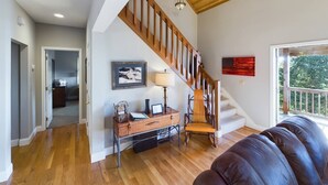 Un amplio salón con una escalera de madera, un sofá de cuero y un escritorio con lámpara.