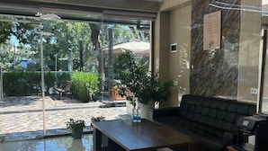 A modern lobby with a glass entrance, a sofa, a coffee machine, and a potted plant. - Artist Regency Hotel (Tashkent)