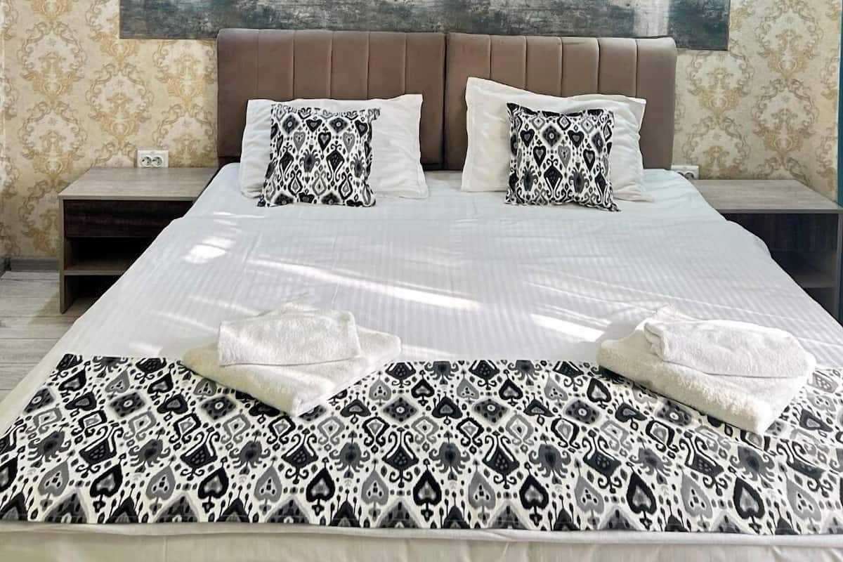 A hotel room with a large bed, two nightstands, a modern headboard, patterned wallpaper, and a large abstract painting on the wall.