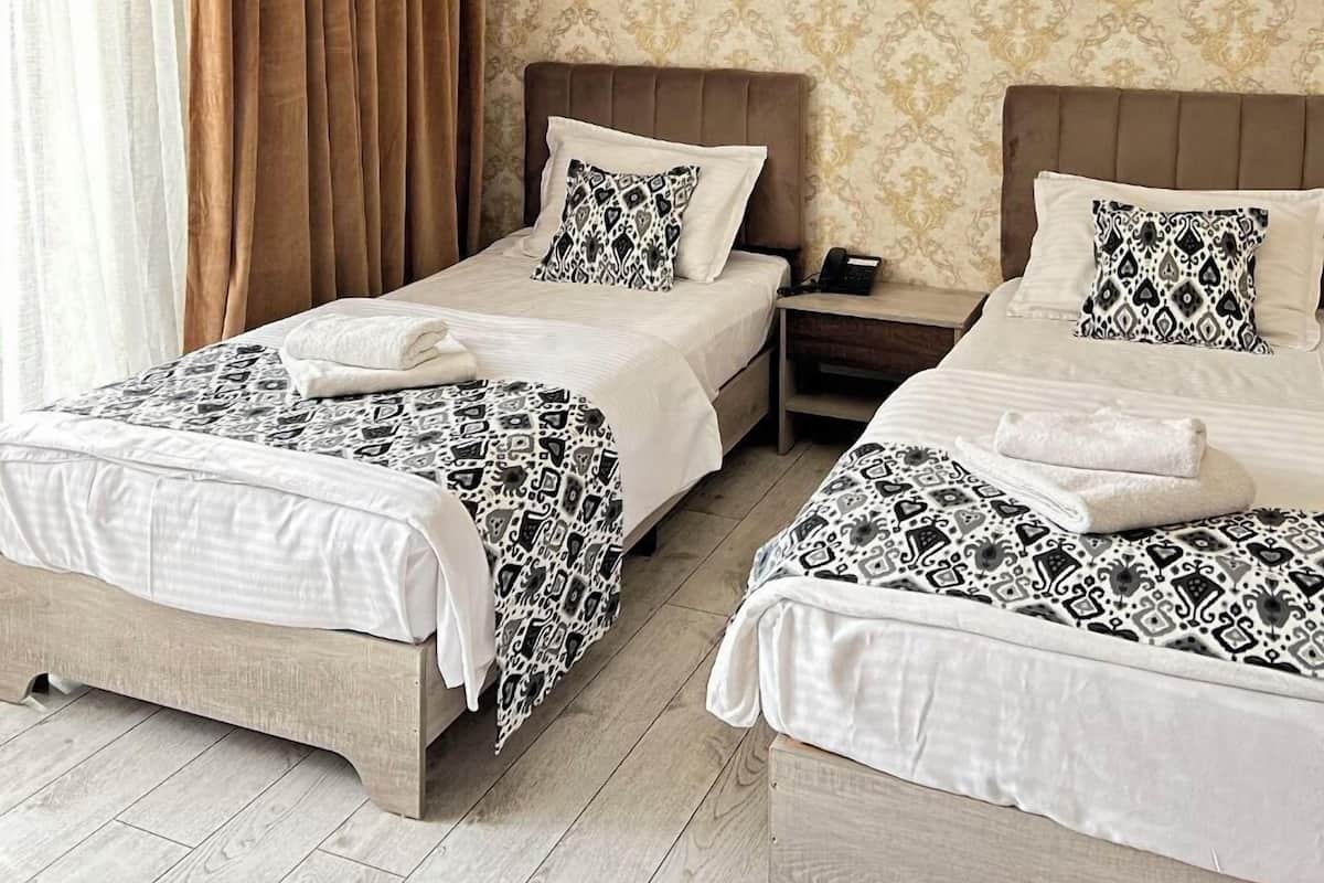 A hotel room with two beds, a nightstand, a lamp, and a patterned wallpaper.