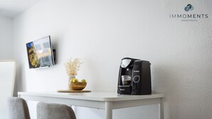 Una cucina moderna con una moka, una ciotola di frutta e un vaso di fiori secchi su un piano di lavoro bianco.