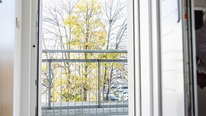 Une vue depuis un balcon doté d’une rambarde en métal, donnant sur une rue où sont garées des voitures et où l’on aperçoit des arbres aux feuilles jaunes.