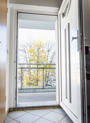 A view from a balcony with a metal railing, looking out onto a street with parked cars and trees with yellow leaves.