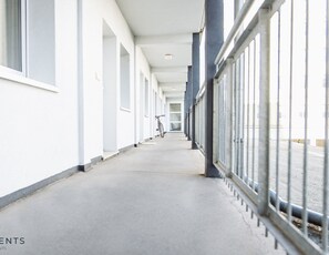 A corridor with a bicycle leaning against the wall, white walls, and a metal railing on the right.