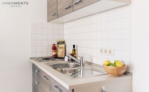A modern kitchen with white tiles, stainless steel appliances, and wooden cabinets.
