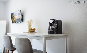 A modern kitchen with a coffee maker, a bowl of fruit, and a vase of dried flowers on a white countertop.