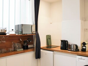A kitchen with a microwave, toaster, and coffee maker on the counter, a dishwasher below, and a window with curtains. - Nice Studio Near Eiffel Tower (Paris)
