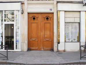 A double wooden door with a plaque above it, a glass door to the left, and a window with curtains to the right.