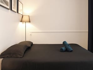 A single bed with a dark-colored mattress and a rolled towel on it. - Nice Studio Near Eiffel Tower (Paris)