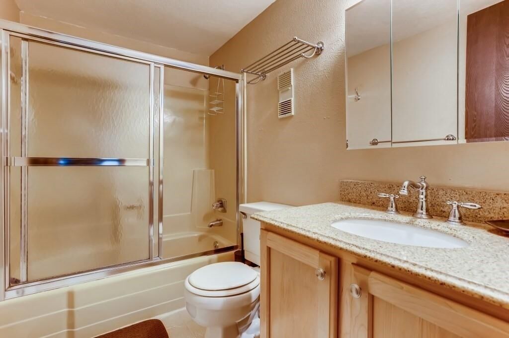 A bathroom with a glass shower enclosure, a toilet, a sink with two faucets, and a mirror above the sink.