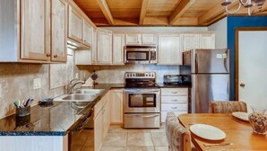 A kitchen with wooden cabinets, stainless steel appliances, a marble countertop, and a dining area with a wooden table and chairs.