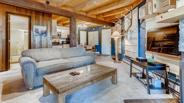 A cozy living room with a sofa, coffee table, and a kitchen area with wooden cabinets and a hanging light fixture.