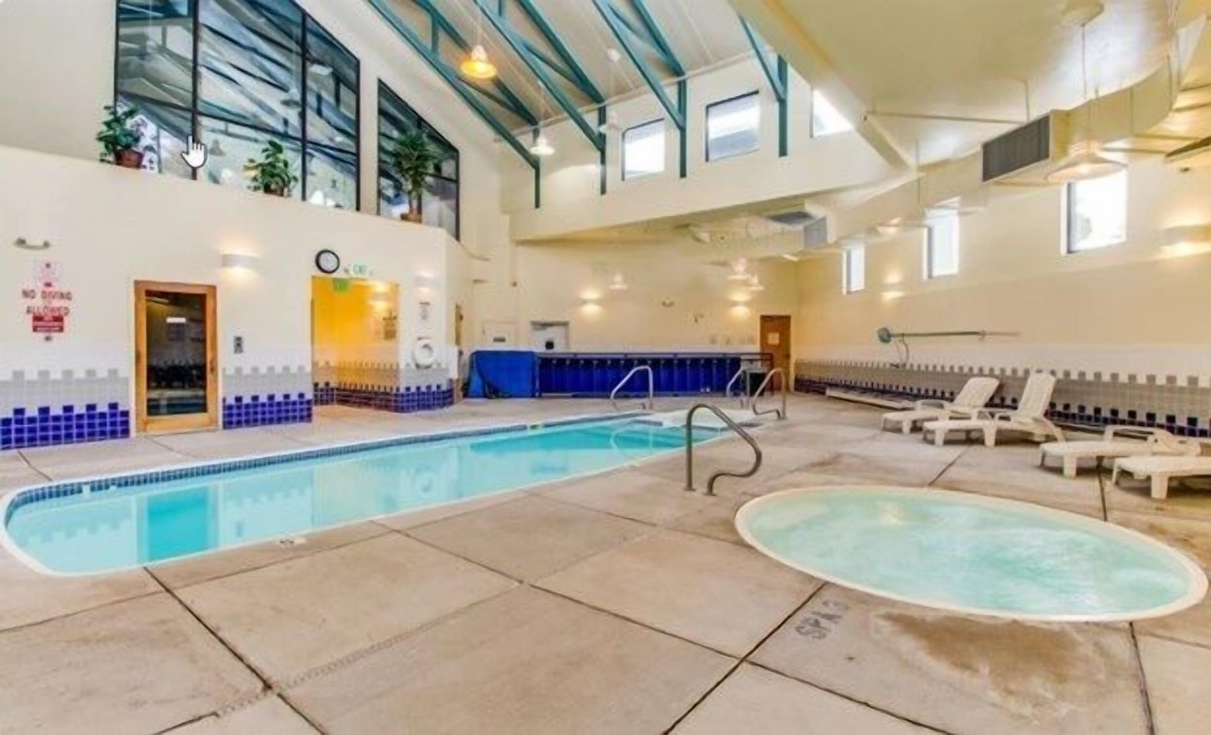 Una piscina interior con suelo de baldosas, un jacuzzi y sillas de descanso.