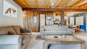 A cozy living room with a wooden ceiling, a grey sofa, a wooden coffee table, and a painting of a dog on the wall.