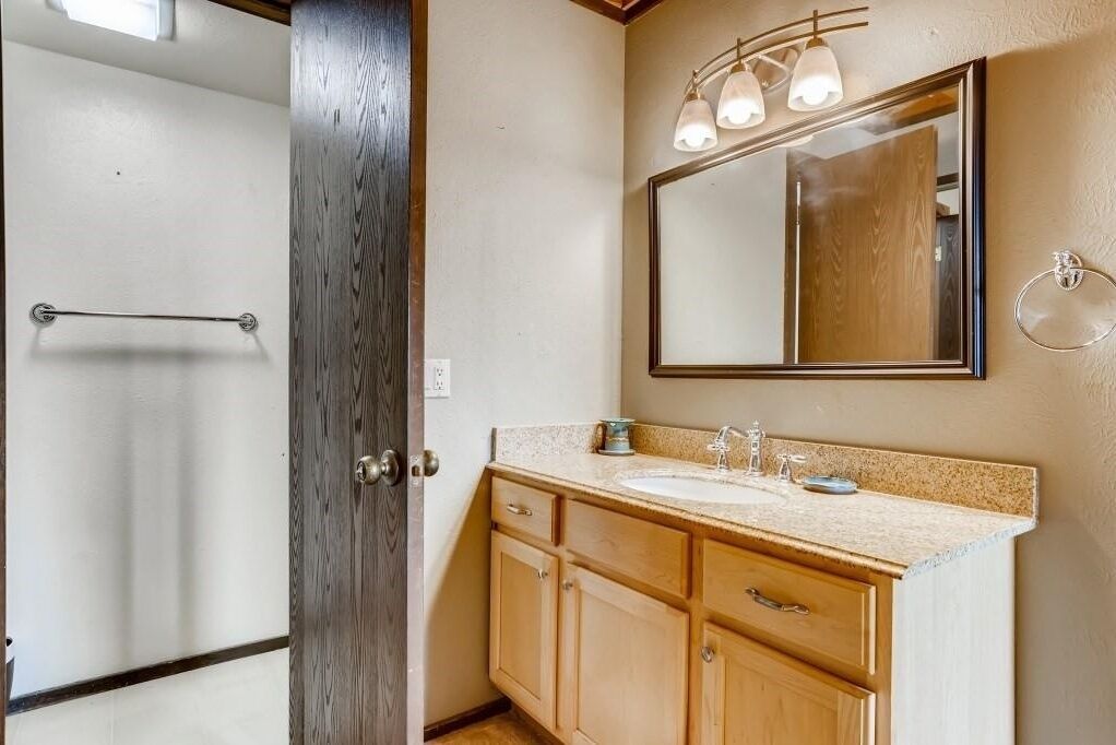 A bathroom with a wooden door, a sink with a mirror above it, and a towel rack.