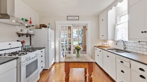 A modern kitchen with white cabinetry, a wooden floor, a central island, and a view to the backyard. - Reizend Haus 2 Bedroom Home by RedAwning (Fredericksburg)