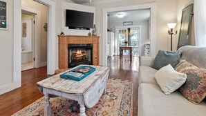 A living room with a fireplace, a television mounted above it, and a sofa with decorative pillows. - Reizend Haus 2 Bedroom Home by RedAwning (Fredericksburg)
