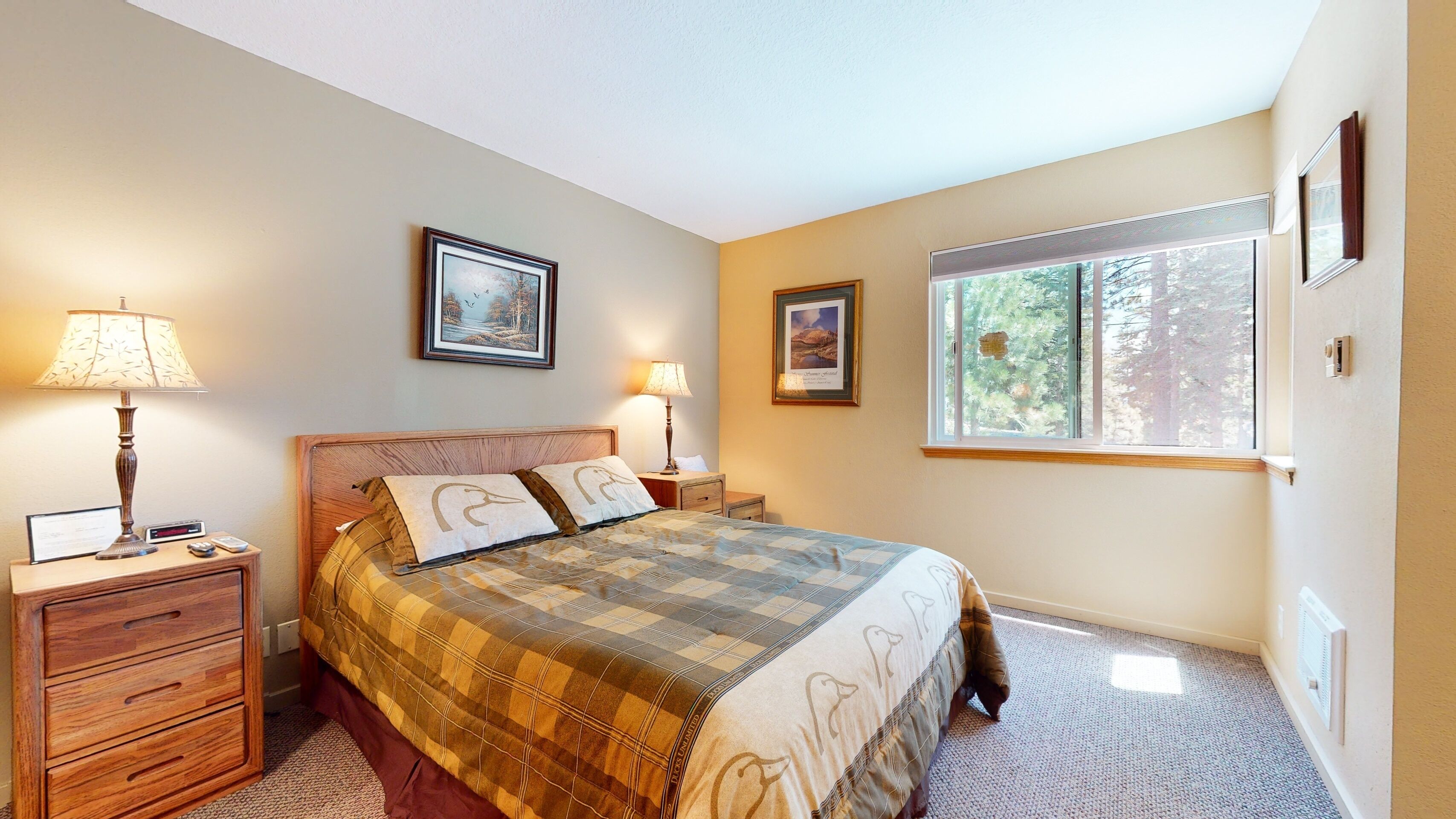 A bedroom with a bed, two bedside tables, a nightstand, a window, and two wall-mounted lamps.