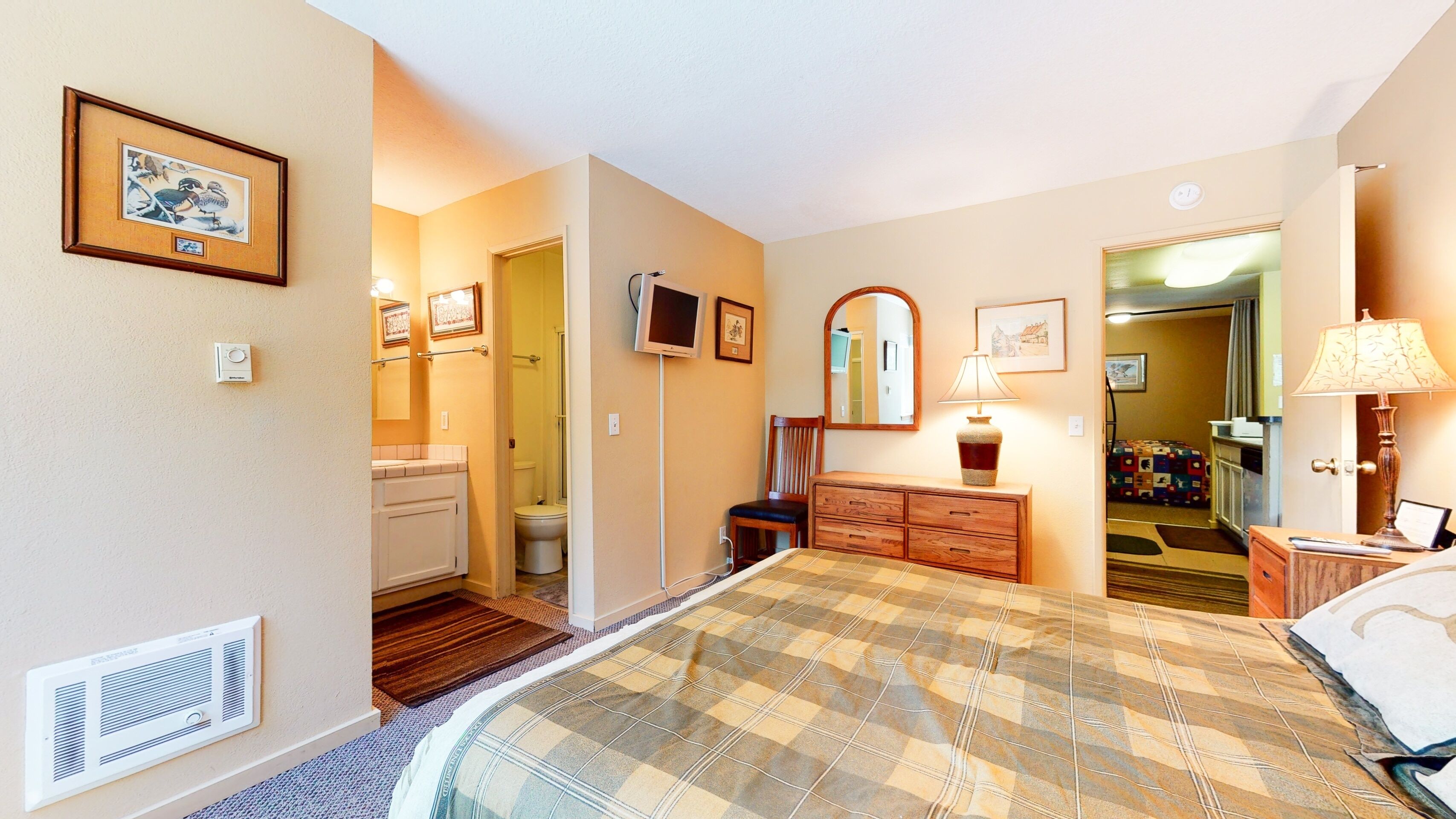 A bedroom with a bed, dresser, mirror, and a bathroom visible through an open door.