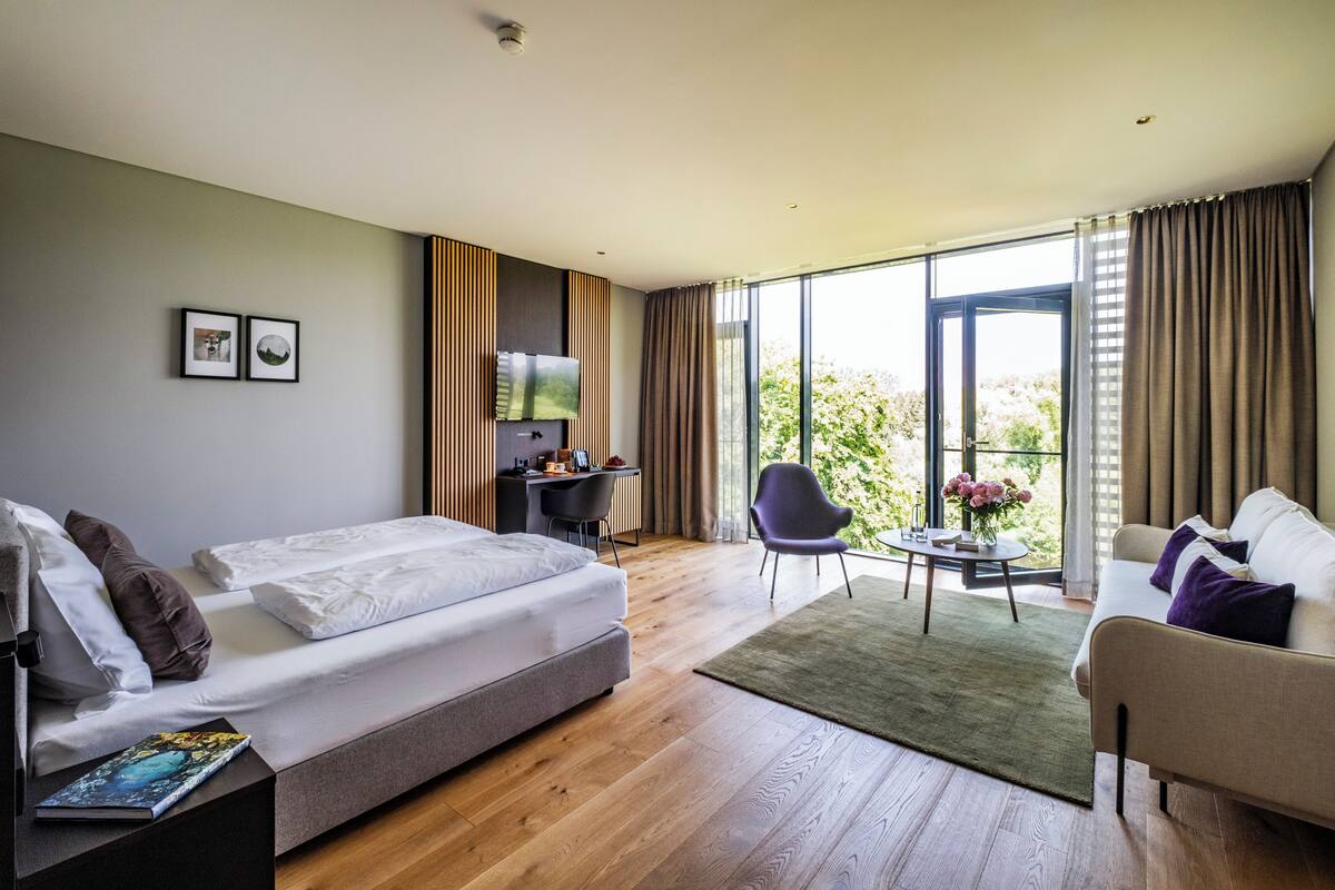 A modern hotel room with a bed, a desk, a chair, and a sofa.