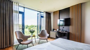 A modern hotel room with a large bed, two armchairs, a desk, and a TV. - Hotel Breitenburg (Breitenburg)
