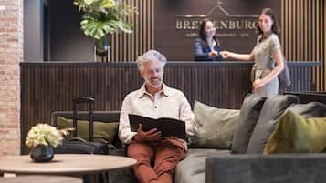 A man sitting on a sofa reading a book in a modern lobby with a reception desk and a brick wall.