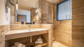 A modern bathroom with a large mirror, a sink, and a shower. There are towels and a toothbrush on the sink counter.