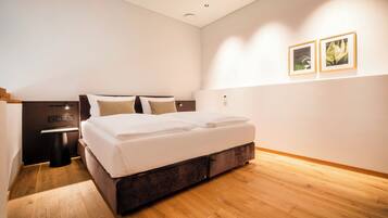 A modern bedroom with a wooden floor, a large bed with white linens, a bedside table, and two framed pictures on the wall.