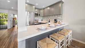 A modern kitchen with stainless steel appliances, a white island with bar stools, and a view of the outdoors.