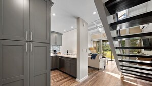 A modern kitchen with grey cabinets, a wooden floor, and a staircase leading to a balcony.