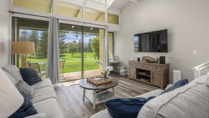 A modern living room with a large sliding glass door leading to a patio, a flat-screen TV mounted on the wall, and a cozy seating area with a sofa and a coffee table.