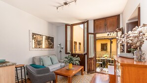 Un salon avec un canapé, une table basse et des tabourets de bar. Il y a un tableau au mur et une fenêtre avec des rideaux.
