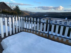 Cubierta nevada con valla de piquetes blancos, con vistas a un paisaje montañoso con casas y árboles.